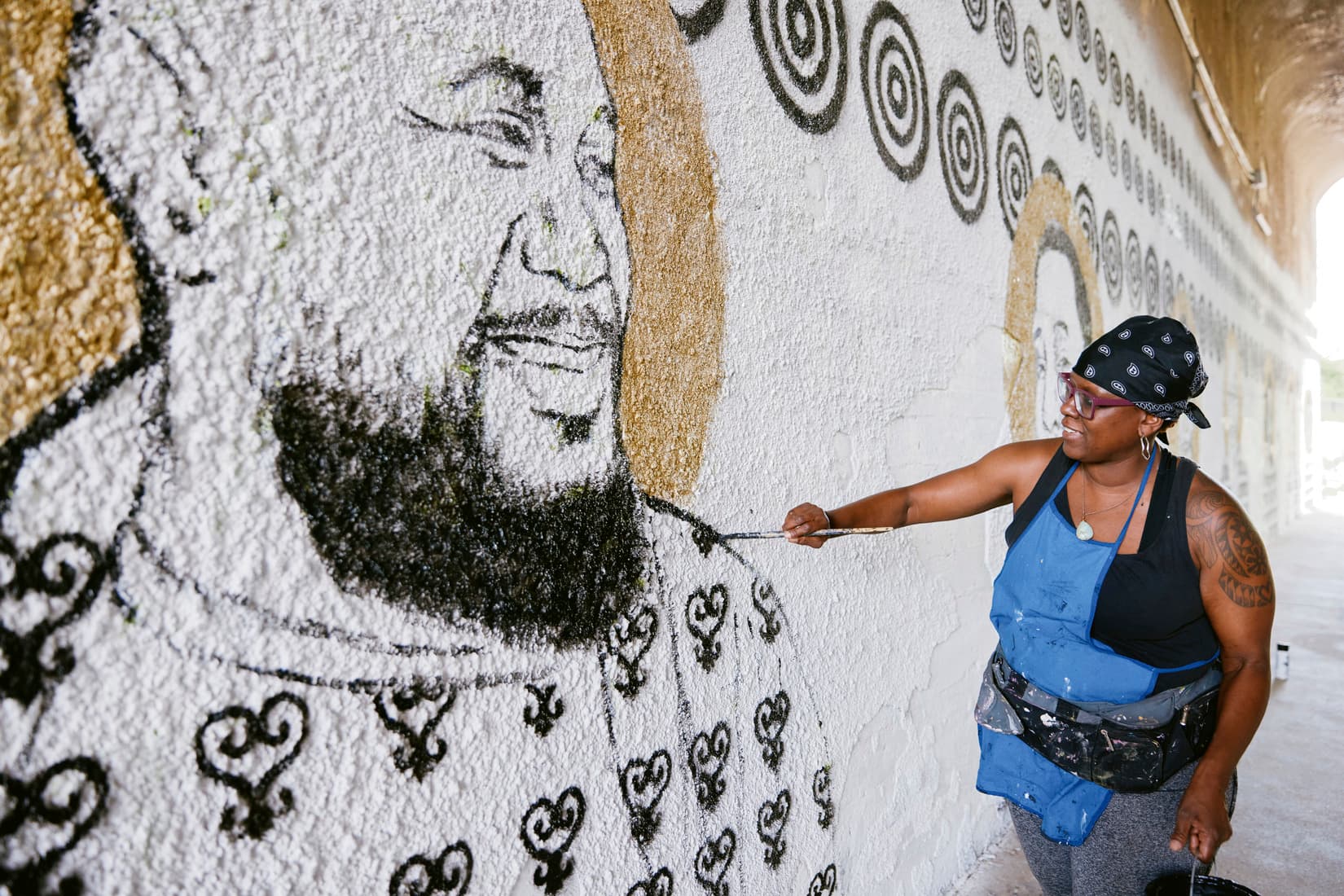 A woman paints a mural on a wall.